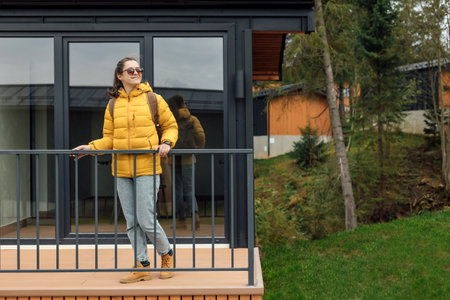 Young female in yellow down jacket stands outdoor near modular cabin housesの写真素材