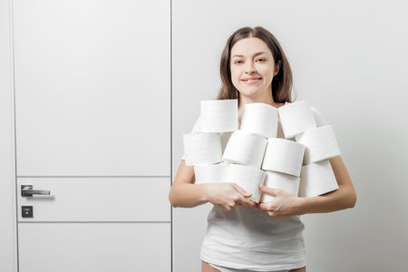 Woman in white t shirt holds a pyramid of toilet paper rolls in hands on white color backgroundの写真素材