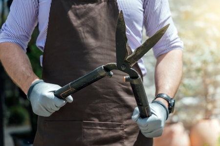 Stylish man-gardener with garden scissors in hand standing in front of garden houseの写真素材