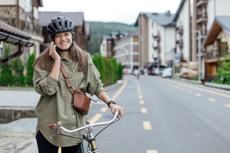 Woman cyclist talks on smartphone while stop on the bicycle road path in city