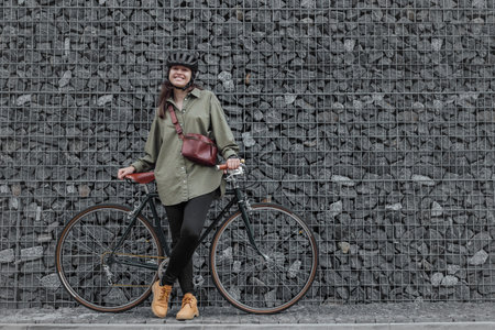 Woman cyclist stand with bicycle near stone wall in urban streetの写真素材
