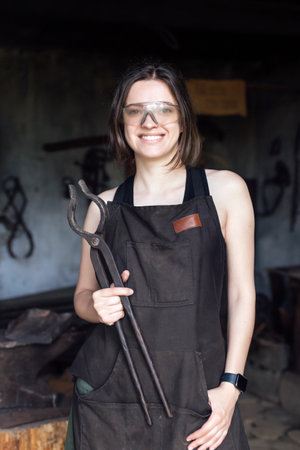 Young woman blacksmith portraitin protective glasses in workshopの写真素材