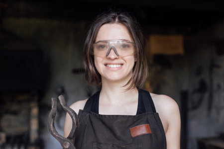 Young woman blacksmith portraitin protective glasses in workshopの写真素材