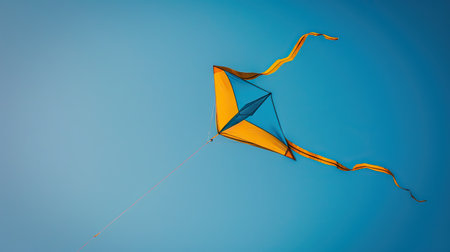 A yellow and blue kite flying high against a clear blue skyの素材