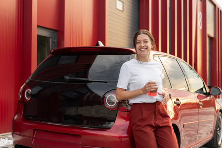 Attractive woman drinks fresh lemonade with red car on urban backgroundの写真素材