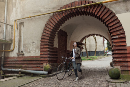 Woman in retro tweed outfit cycling through historic British streets during a sunny dayの写真素材