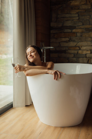 Enjoying a relaxing moment in a modern bathtub with a drinkの写真素材