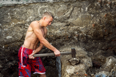 Sports guy with a hammer works in an earthen pitの写真素材