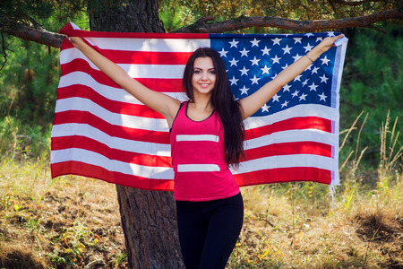 Beautiful model poses with the flag of the United States in the summer parkの写真素材