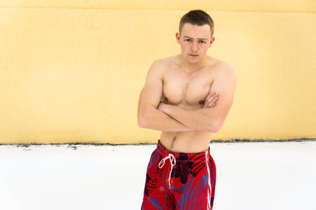Sports guy without clothing in winter snow. Hardening in winter season. Frosty weather. Yellow wall on background.の写真素材