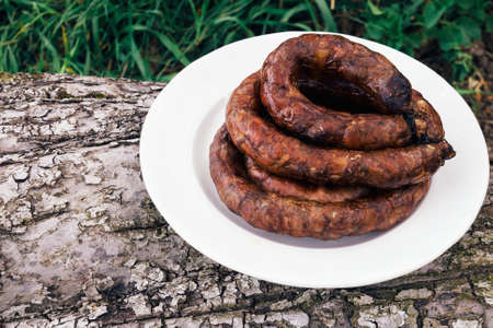 Grilled sausage in a white bowl onwooden stump