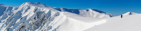 Panorama of snow-covered rocks of the mountain range. A man standing in the snow at the edge of the...