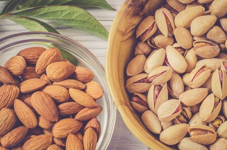 Almonds and pistachios in bowls close-up. Dress pistachios and almond kernels on a light background with green leavesの写真素材