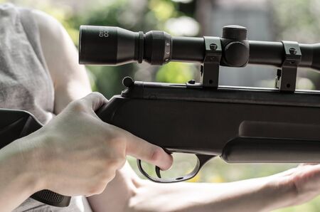 A man holds an air rifle with an optical sight in his hands. The hunter with a gun in his hands