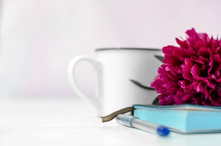 The flower lies on a notebook. Pen and notebook close-up. White cup in the backgroundの写真素材