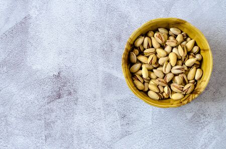 Brown bowl with shell pistachios on a gray background. Healthy eating concept