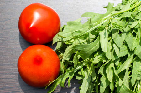 Arugula and two red tomatoes on a brown wooden background in direct sunlight. Healthy eating conceptの写真素材