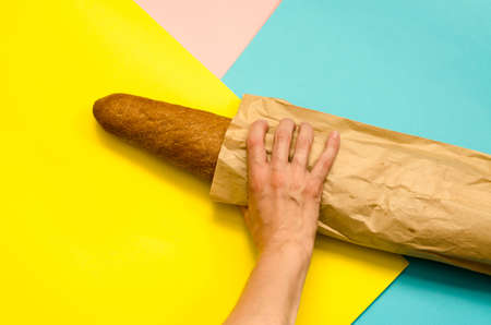 Hand holds rye baguette in a paper bag. Bread in a bag on a colorful background. Bakery products
