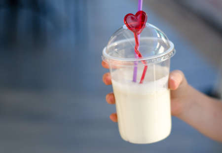 The child's hand holds a plastic glass with a milkshakeの写真素材