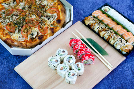 A lot of different sushi rolls and a big pizza in a box. Sushi rolls, green leaf and sticksの写真素材