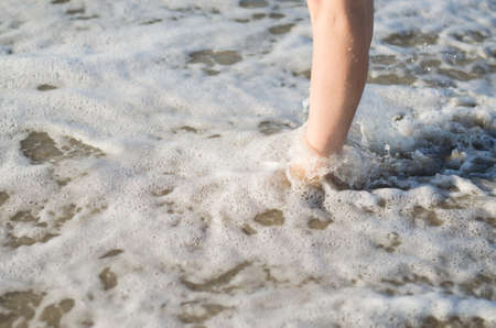 Women's legs are covered by the sea wave. Feet in the water close-up.の写真素材