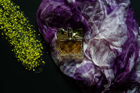 Women's perfume, purple and white scarf and yellow beads on a dark background. Female beauty concept.の写真素材