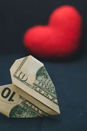 A heart made of paper money in the foreground and a red heart in the backgroundの写真素材