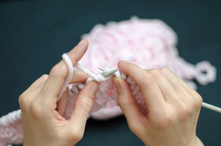 A young girl knits something with pink threads
