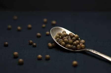 Black pepper peas on a black background in a spoon and in bulk