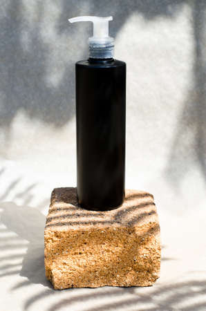 A black bottle with a dispenser stands on a stone on a beige background with shadows. Cosmetics