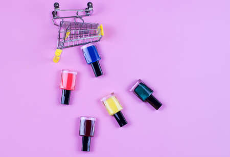 Different colors nail polishes and a shopping trolley on a pink background. beauty and fashion trendy concept. flat lay, top viewの写真素材