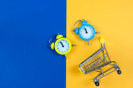 Clock and shopping basket on a yellow-blue background.の写真素材