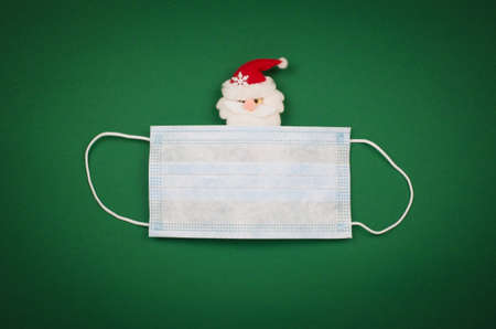 Toy Santa Claus in a protective medical mask on a green background.