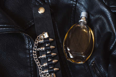 a bottle of women's perfume on a black leather jacket. Women's perfume and leather bracelet with bulletsの写真素材