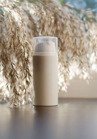 Beige cosmetic bottle against a background of reed flowers. Beauty concept