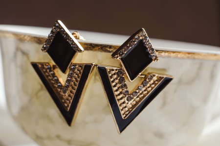 Triangle earrings hang from the edge of a beige cup. Bijouterie jewelryの写真素材