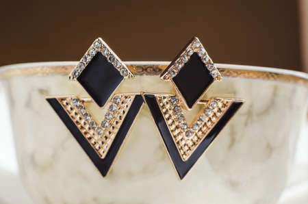 Triangle earrings hang from the edge of a beige cup. Bijouterie jewelry