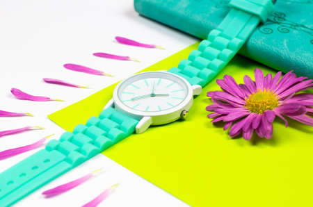 A mint-colored watch is on a notebook. Notepad and clock with flower petals