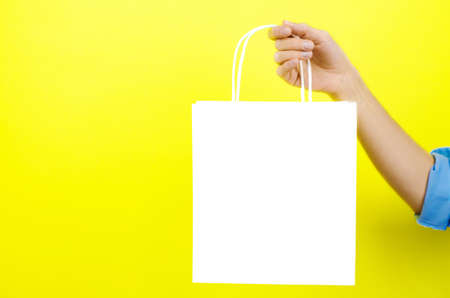 White paper bag in a female hand on a yellow backgroundの写真素材