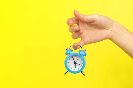 Small blue alarm clock hanging on the finger of a female hand