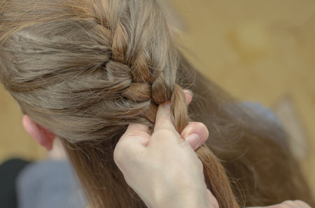 A woman braids a pigtail for a red-haired girl. Hair weaving hairstyles. Braiding close up