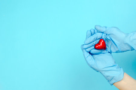 Hands in blue medical gloves hold a heart on a blue background. Health care concept. World heart dayの写真素材