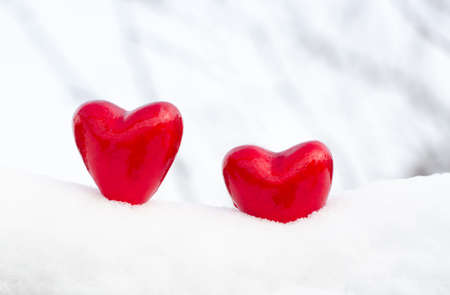 Two red hearts in the snow on a light background.
