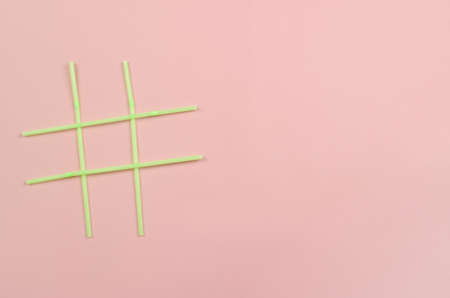 Hashtag symbol of green plastic beverage straws on pink background