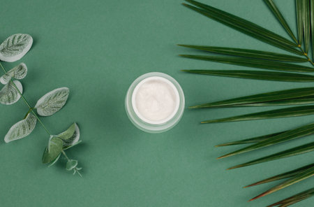 Top view of an open jar of cream and green leaves on a colored background. Beauty concept with cosmetic products for the face.の写真素材