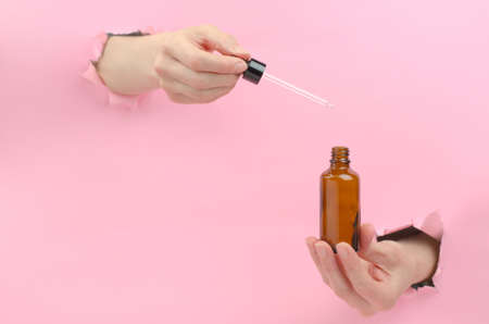 Female hands hold a bottle with a pipette. A woman draws serum or essential oil from a brown bottle with a pipette. Beauty SPA conceptの写真素材