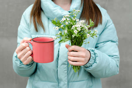 Unrecognizable woman in a menthol jacket holds a cup and a bouquet of wildflowersの写真素材