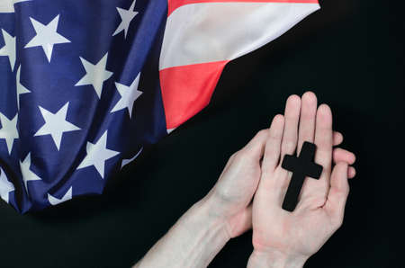 Cross in male hands against the background of the American flagの写真素材