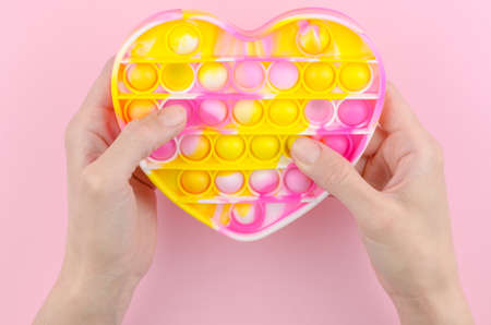 Pop it in the shape of a heart on a pink background. Children's modern toy pop it fidget in female hands. Silicone toy for the development of fine motor skills.の写真素材