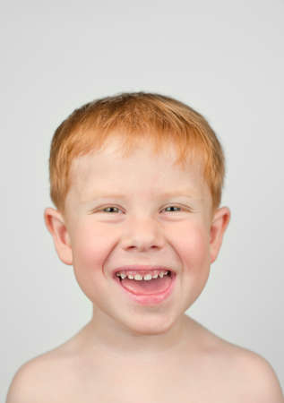 Close up portrait of 4 year old redhead boy. The boy looks at the camera and laughs on a gray...